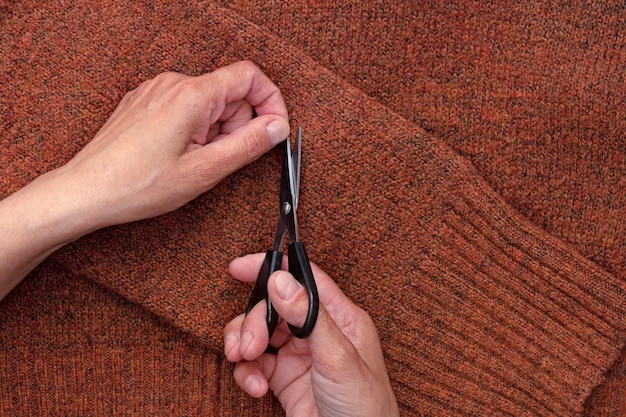 Mani che tagliano la lanugine dal tessuto di lana usando le forbici