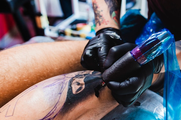 Mani che tatuano sulla gamba con la macchina