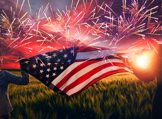 Mani che tengono bandiera americana al tramonto con fuochi d'artificio del 4 luglio giorno dell'indipendenza