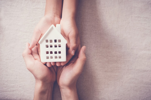 mani che tengono casa bianca, casa di famiglia e concetto di rifugio per senzatetto