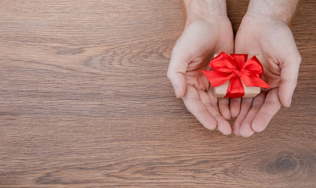 Mani che tengono confezione regalo con fiocco rosso regalo su sfondo di legno