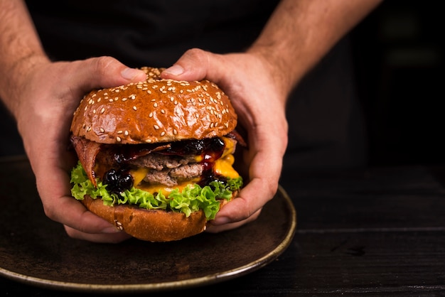 Mani che tengono doppio hamburger con formaggio