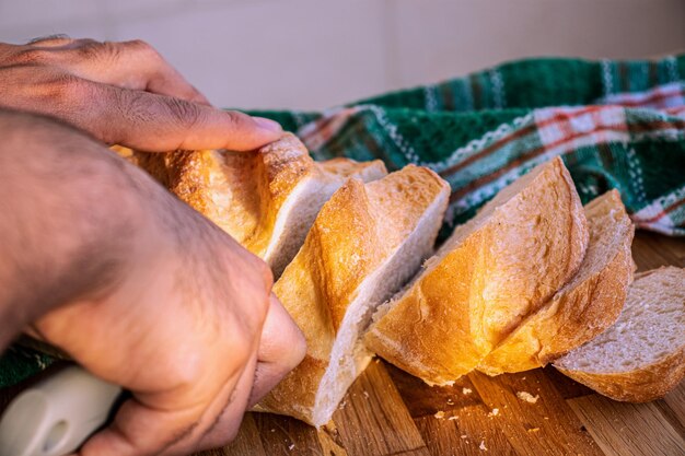 Mani che tengono il coltello e tagliano il pane a fette da servire