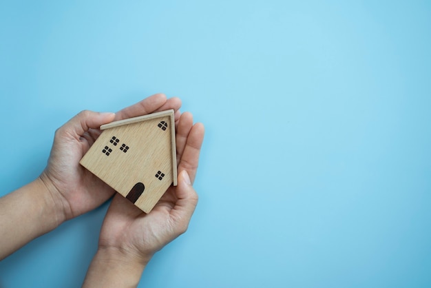 Mani che tengono il legno della vecchia casa su sfondo blu pastello home proteggendo il concetto di assicurazione