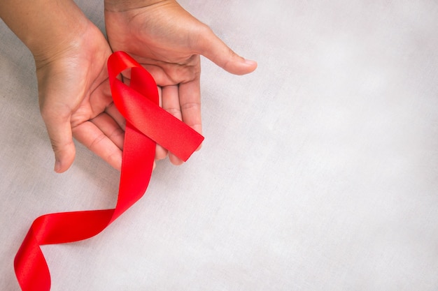 Mani che tengono il nastro rosso su tessuto bianco con copia spazio simbolo per la solidarietà delle persone che vivono con l'HIVAIDS e per la consapevolezza e la prevenzione dell'abuso di droghe e della guida ubriaca Concetto di salute