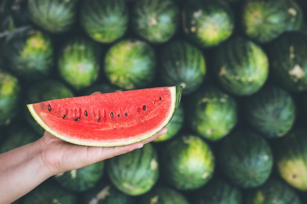 Mani che tengono il pezzo di anguria fresca fetta rossa sullo sfondo del mucchio