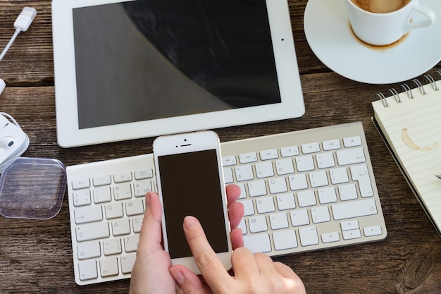 Mani che tengono il telefono sul tavolo da lavoro in legno con tastiera e tablet