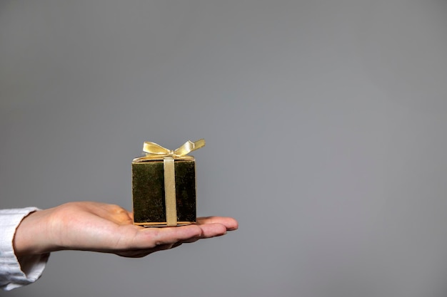 Mani che tengono la confezione regalo d'oro isolata su sfondo grigio che dà il presente compleannochristmasmothersday o