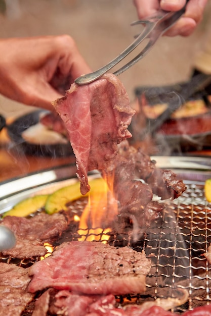 Mani che tengono le pinze per grigliare la carne sul fornello yakiniku cibo popolare a buffet