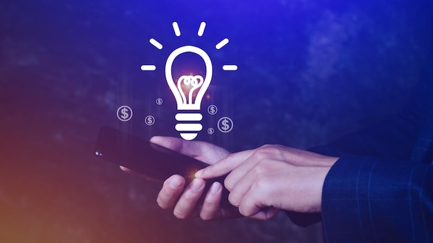 Mani che tengono lo smartphone con la lampadina Idea luminosa lampadina per il concetto nuovo concetto di idea con tecnologia di innovazione e ispirazione nel concetto di scienza e comunicazione