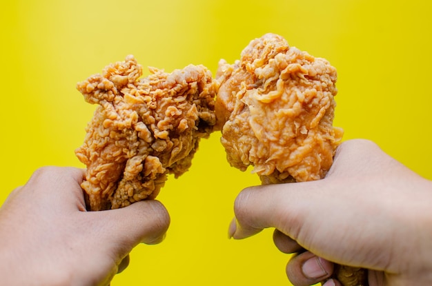 Mani che tengono pollo fritto isolato su sfondo giallo gustoso bastone di pollo fritto croccante