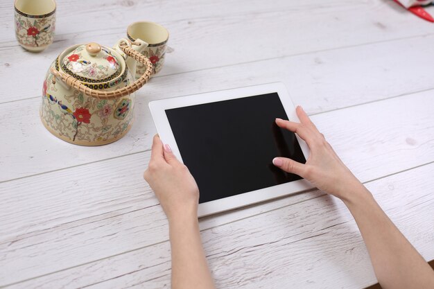 Mani che tengono tablet simile allo stile ipades su un tavolo di legno con tè