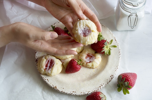 mani che tengono un biscotto ripieno di marmellata di fragole