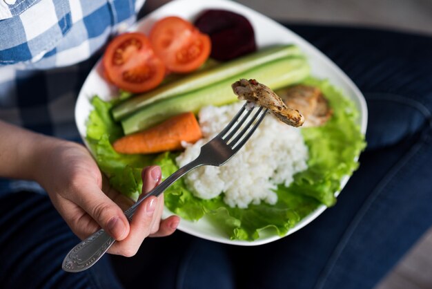 Mani che tengono un piatto con verdure e pollo