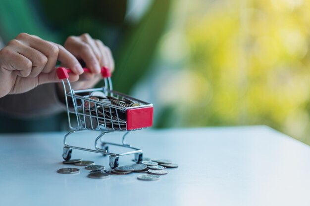 Mani che tengono un piccolo carrello pieno di monete per risparmiare denaro e concetto finanziario