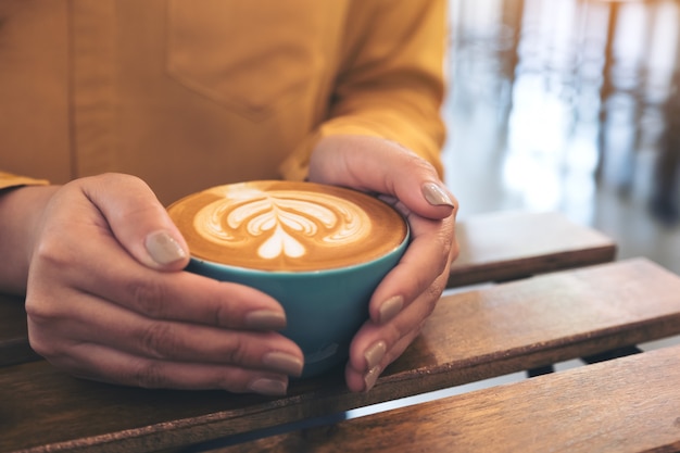 Mani che tengono una tazza blu del caffè caldo del latte