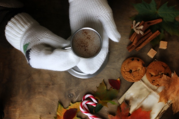 Mani che tengono una tazza di caffè caldo su un tavolo con foglie d'autunno