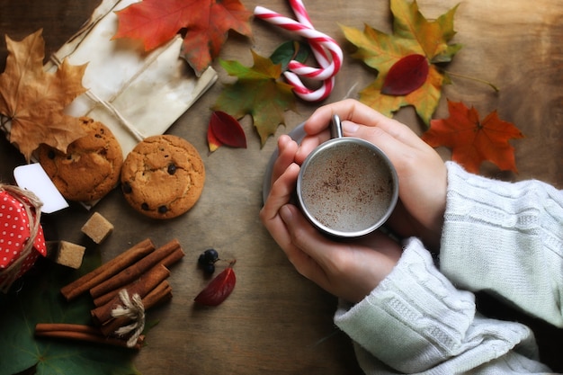 Mani che tengono una tazza di caffè caldo su un tavolo con foglie d'autunno