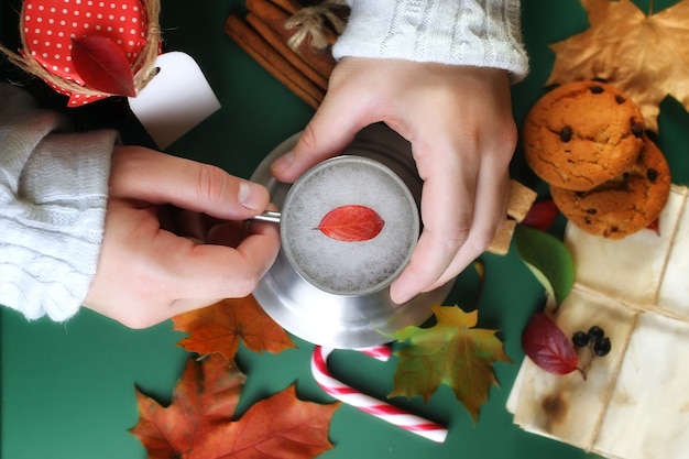 Mani che tengono una tazza di caffè caldo su un tavolo con foglie d'autunno