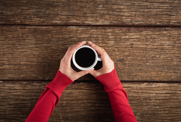 Mani che tengono una tazza di caffè su un tavolo di legno