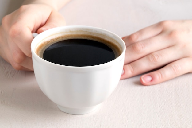 Mani che tengono una tazza di caffè su un tavolo luminoso.