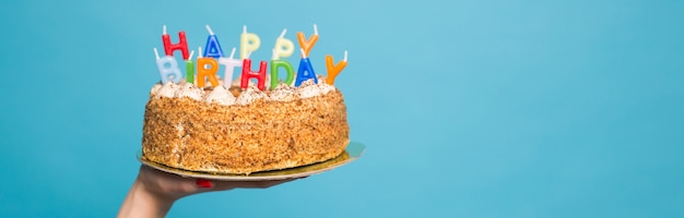 Mani che tengono una torta di compleanno con candele e l'iscrizione compleanno su sfondo blu. Congratulazioni per l'anniversario e il compleanno. Copyspace