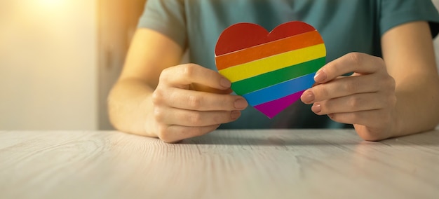 Mani con bandiera color arcobaleno a forma di cuore, simbolo del mese dell'orgoglio LGBT celebrato, comunità di gay, lesbiche, bisessuali e transgender, foto del concetto di diritti umani