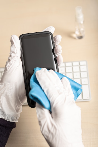 Mani con guanti pulizia cellulare con disinfettante. COVID-19 Concetto di prevenzione della contaminazione da epidemia di coronavirus
