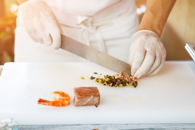 Mani con olive da taglio a coltello. Pezzo di pesce e gamberi. Piccoli pezzi di olive verdi. Dipendente del ristorante che cucina cibo.