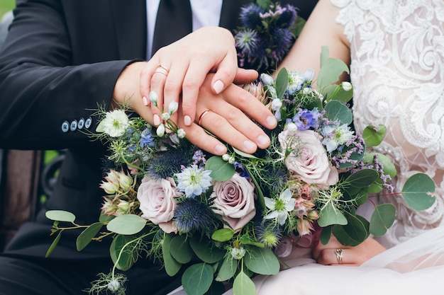 Mani degli sposi con anelli sul bouquet da sposa