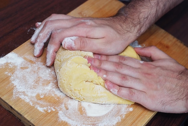 Mani degli uomini che impastano la pasta di pane su un tagliere