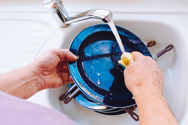 mani degli uomini che lavano i piatti nel lavandino con detersivo