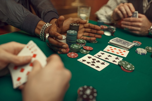 Mani dei giocatori di poker con carte, tavolo da gioco con panno verde nel casinò