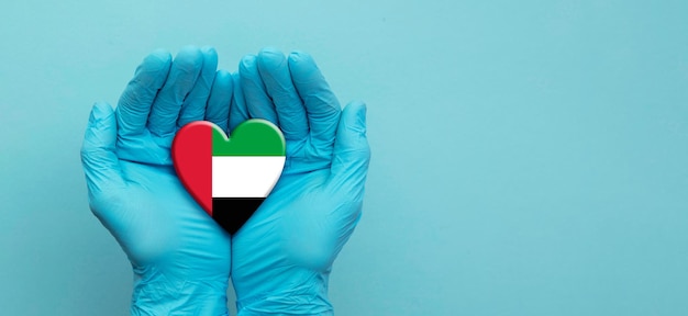 Mani dei medici che indossano guanti chirurgici che tengono il cuore della bandiera degli Emirati Arabi Uniti