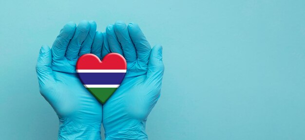 Mani dei medici che indossano guanti chirurgici che tengono il cuore della bandiera del Gambia