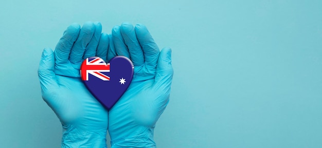 Mani dei medici che indossano guanti chirurgici che tengono il cuore della bandiera dell'australia