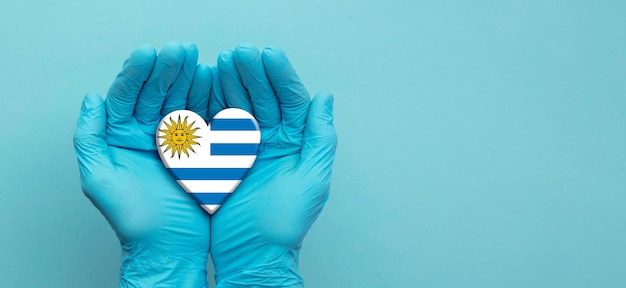 Mani dei medici che indossano guanti chirurgici che tengono il cuore della bandiera dell'Uruguay