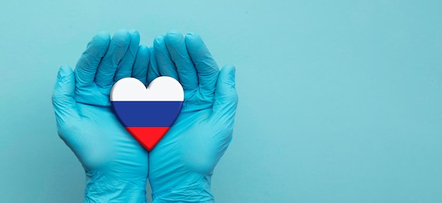 Mani dei medici che indossano guanti chirurgici che tengono il cuore della bandiera della russia