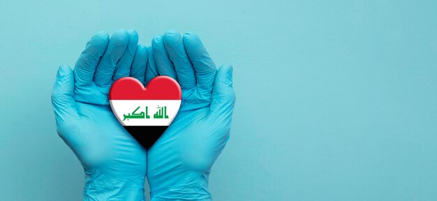 Mani dei medici che indossano guanti chirurgici che tengono il cuore della bandiera irachena
