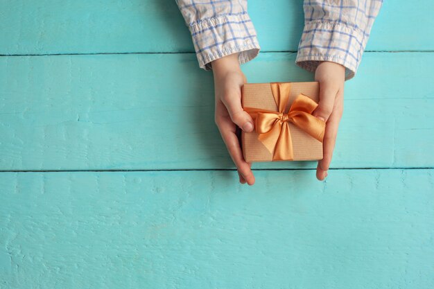 Mani del bambino che tengono confezione regalo avvolto in carta artigianale e legato con fiocco.