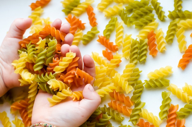 Mani del bambino pieno di pasta a spirale su sfondo bianco