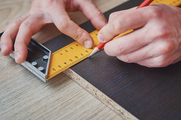 Mani del carpentiere che prendono misura della plancia di legno, primo piano