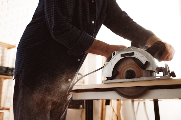 Mani del carpentiere che tagliano il legno con la sega elettrica