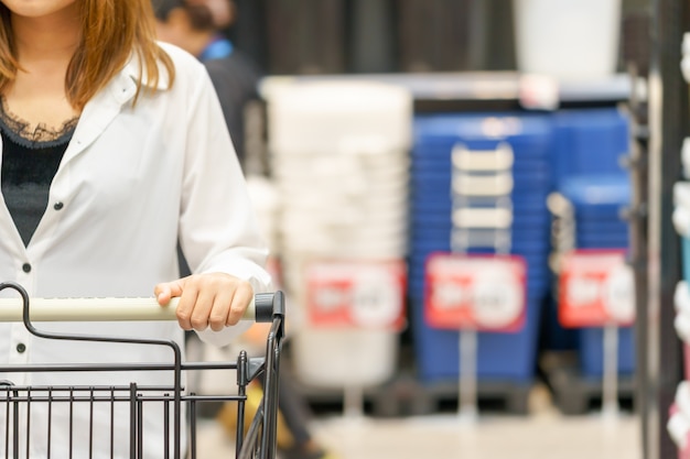 Mani del carrello della spesa della tenuta della donna in supermercato.