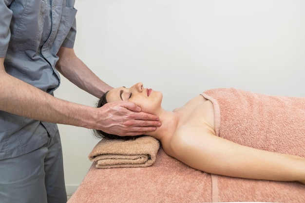 Mani del cosmetologo che fanno massaggio facciale rigenerante rilassante manuale per la giovane donna nel salone di bellezza Massaggio facciale ringiovanente in cosmetologia