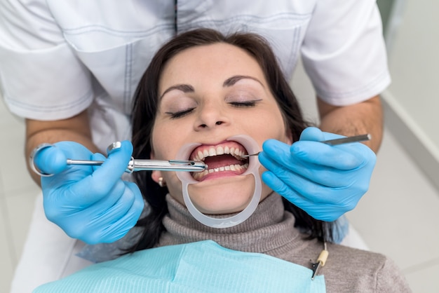 Mani del dentista con strumenti e primo piano del viso del paziente