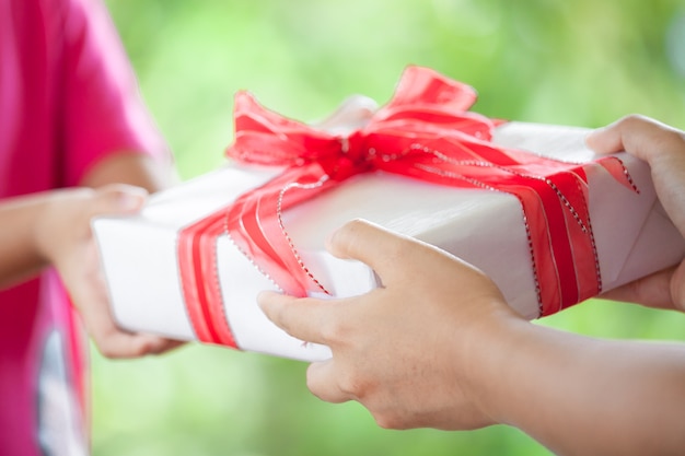 Mani del genitore che dà il regalo di Natale alla ragazza del bambino sul fondo verde della natura. Concetto di Natale