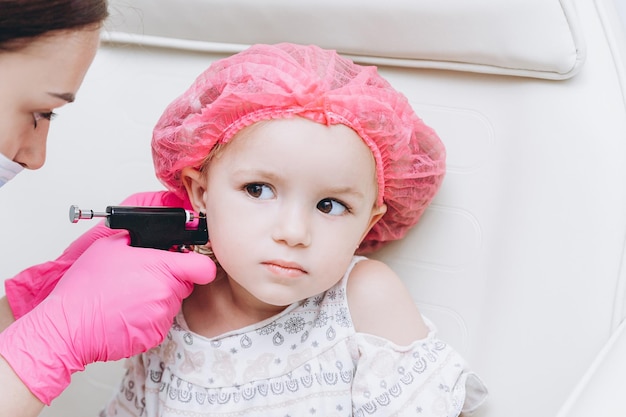 Mani del medico che fanno piercing all'orecchio alla bambina graziosa Copia spazio