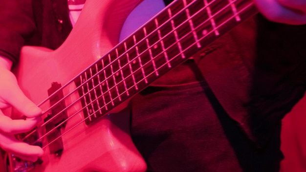 Mani del musicista rock che suona il basso elettrico sulla ripetizione a luce rossa