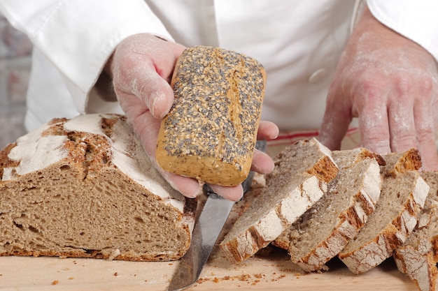 Mani del panettiere con pane fresco sulla tavola di legno